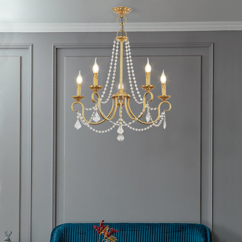 Elegant small brass chandelier illuminating a modern grey paneled room with a teal accent chair.