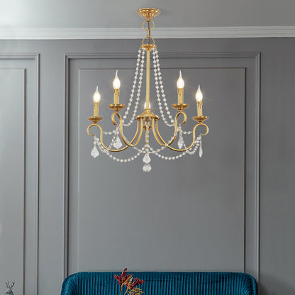 Elegant small brass chandelier illuminating a modern grey paneled room with a teal accent chair.