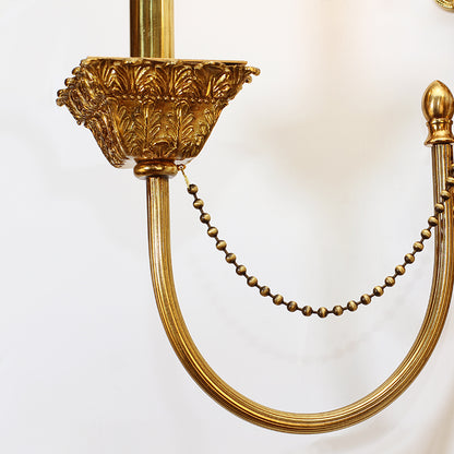 Extreme detail shot of a polished brass bead chain and leaf motif on the luxury hotel corridor light.