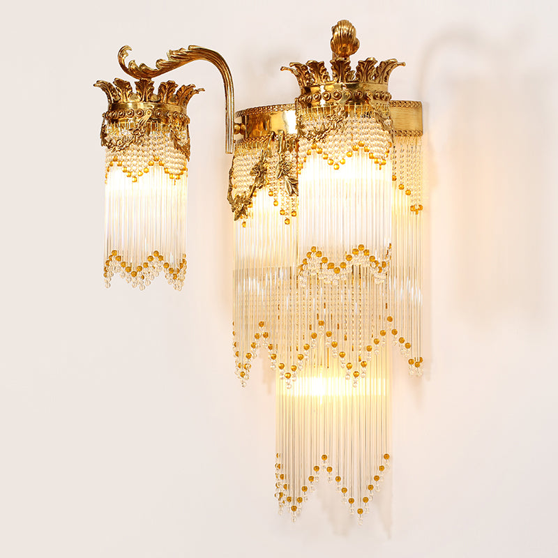 Close-up artistic detail of the brass wall lamp, highlighting the intricate scrollwork and waterfall of clear crystal prisms.
