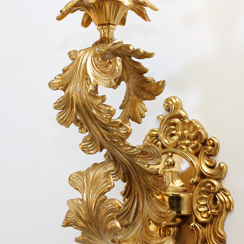 Detailed macro shot of the brass sconce’s exquisite leaf and vine carvings on a white wall.