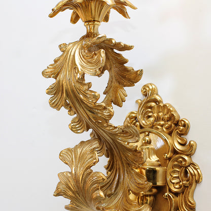 Detailed macro shot of the brass sconce’s exquisite leaf and vine carvings on a white wall.