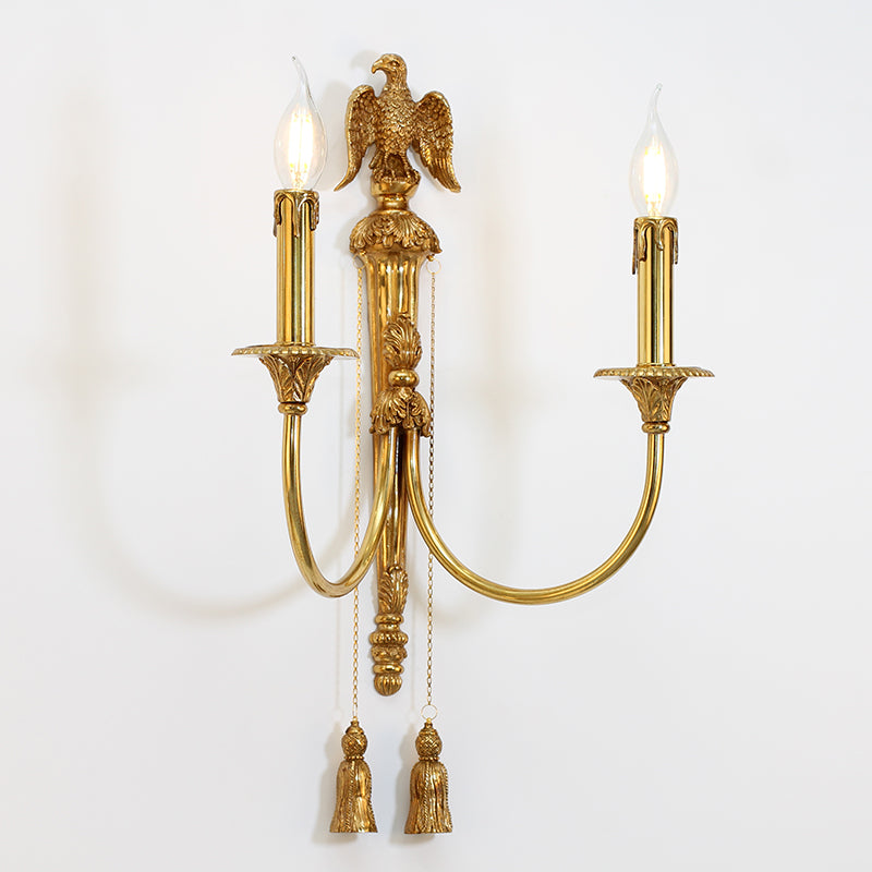 The brass wall sconce emitting a warm glow on a white wall, focusing on the elegant light cast from its candle-style bulbs.