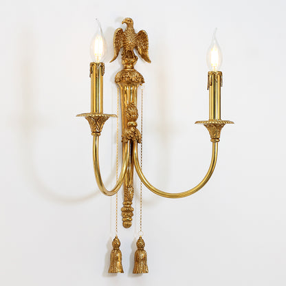The brass wall sconce emitting a warm glow on a white wall, focusing on the elegant light cast from its candle-style bulbs.