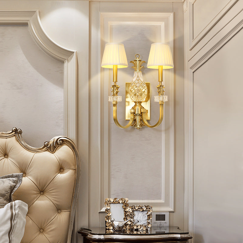 The classical brass wall lamp installed in a luxurious bedroom setting with a tufted headboard and artwork.