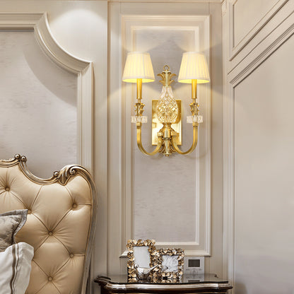 The classical brass wall lamp installed in a luxurious bedroom setting with a tufted headboard and artwork.