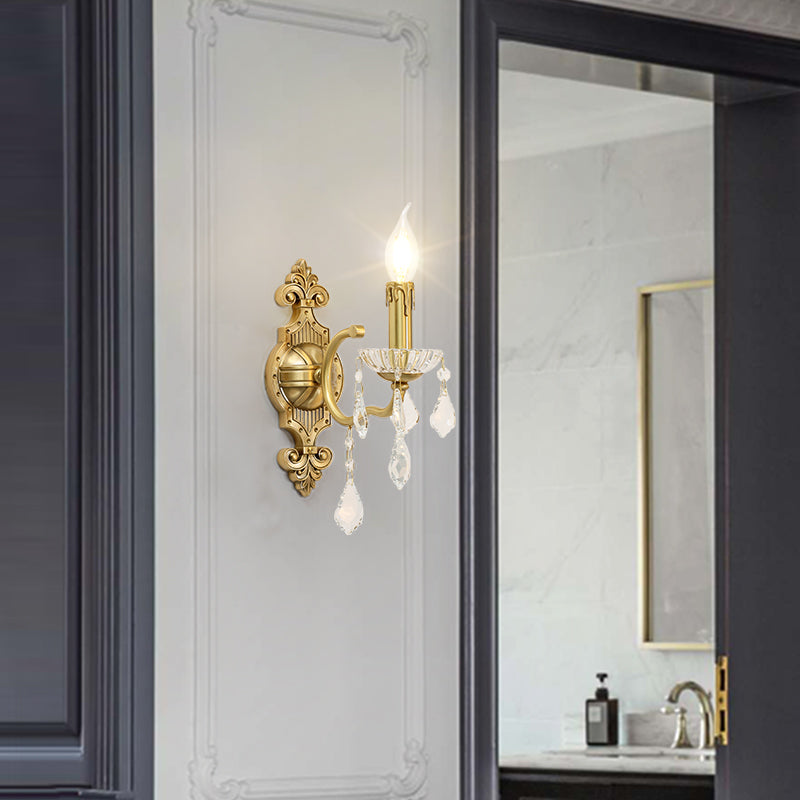 The crystal wall light mounted in a bathroom setting, reflecting in a gold-framed mirror with soft ambient lighting.