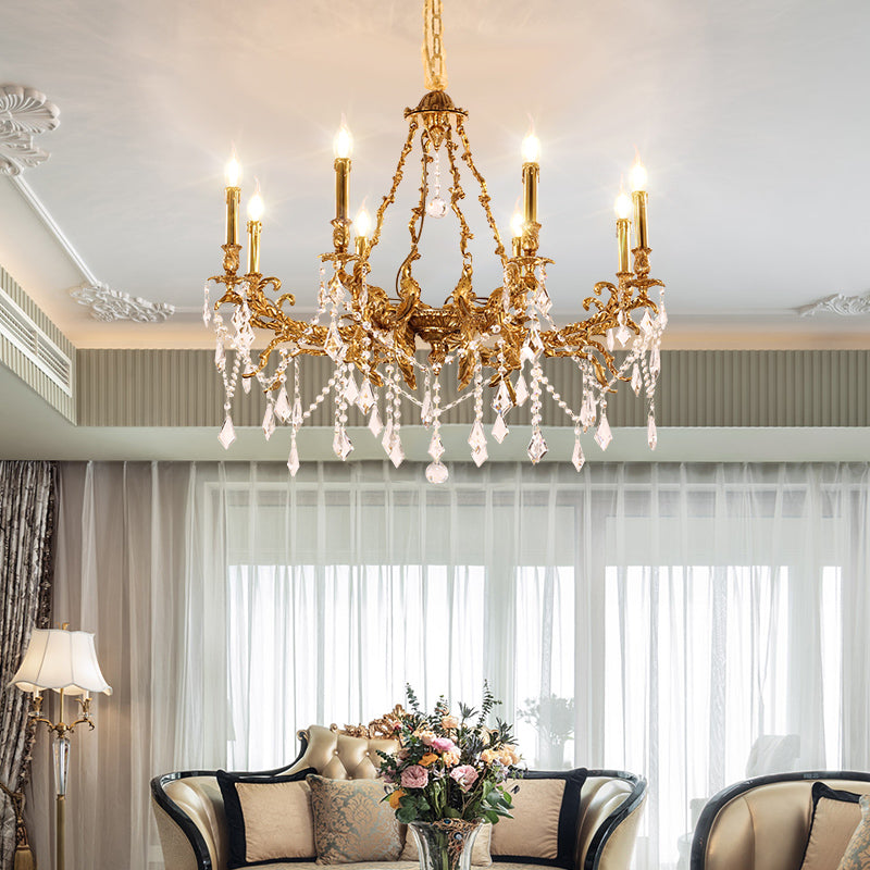 Antique brass chandelier installed in a living room with sofa, pillows, and flowers by a window.